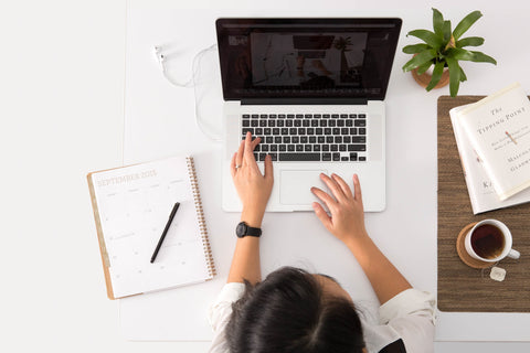 Person sitting and using a laptop next to a planner